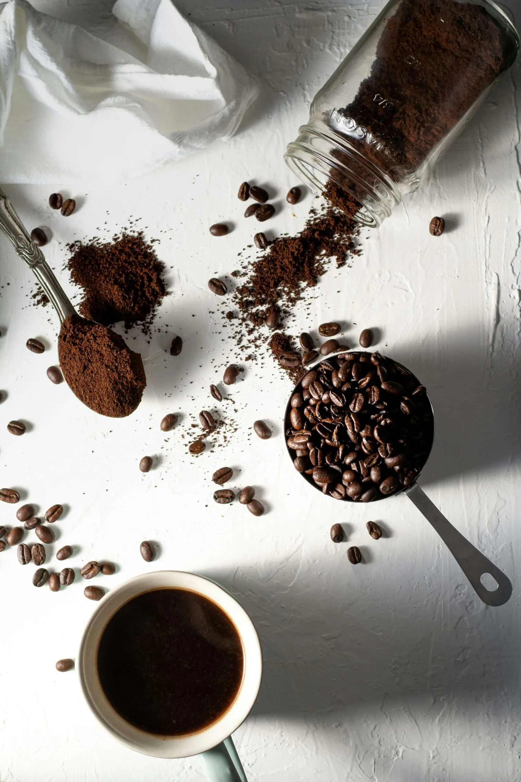Home coffee beans on white ceramic mug beside stainless steel spoon